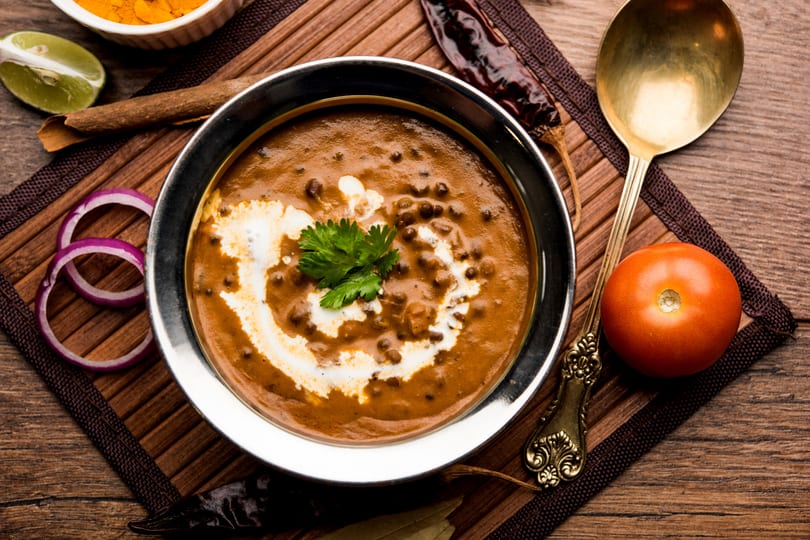 Overhead view of a bowl of creamy Indian Dal Makhani garnished with cilantro and cream, surrounded by spices.